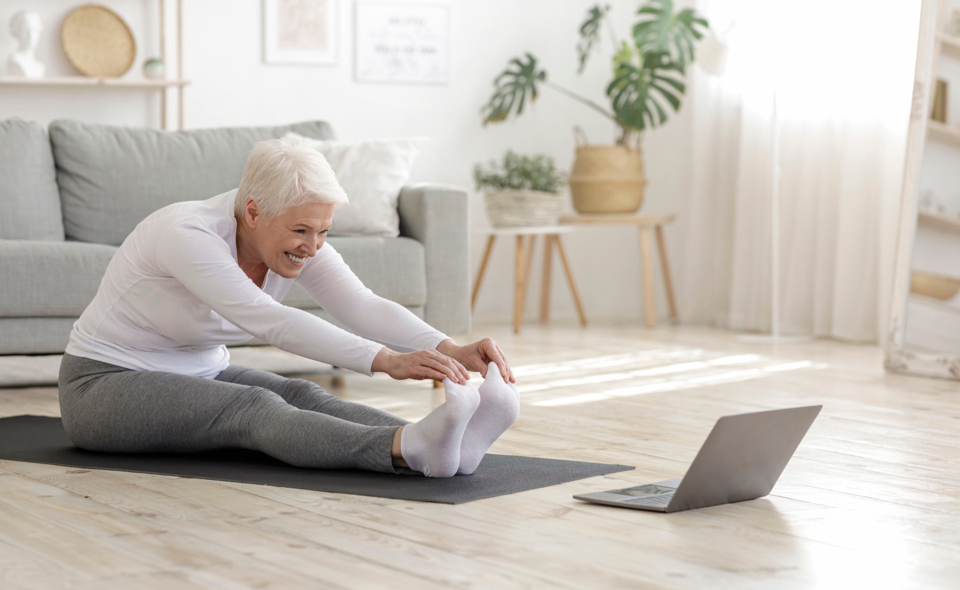 Active senior woman doing stretching exercises In front of laptop