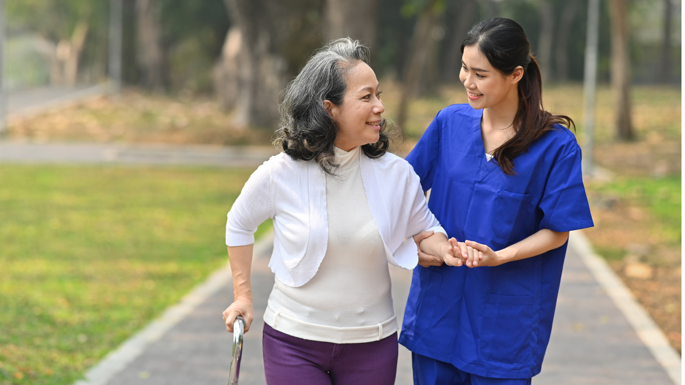 Female healthcare worker assisting senior woman with cane on outdoor walk