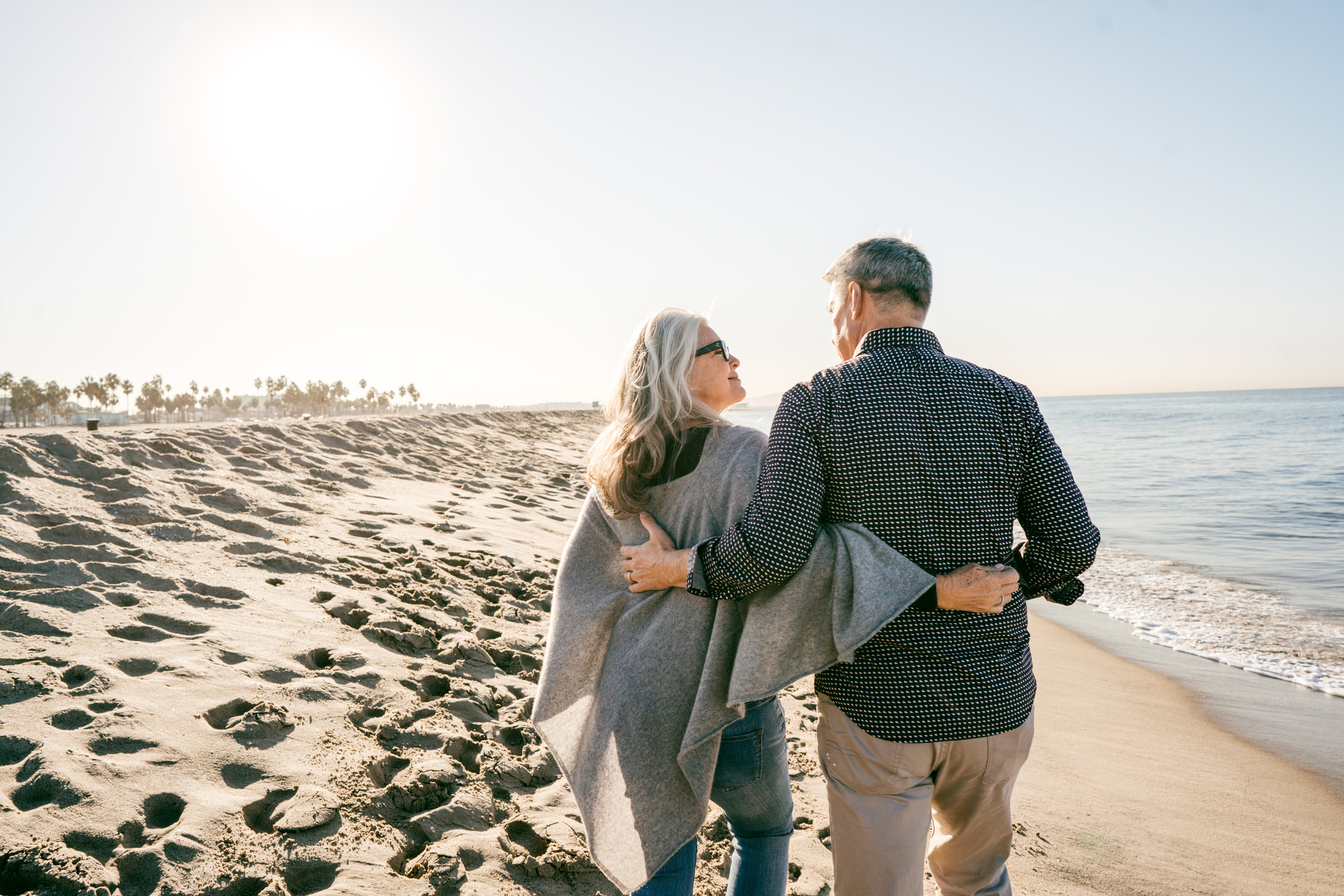 A senior woman and senior man walk side by side on the beach