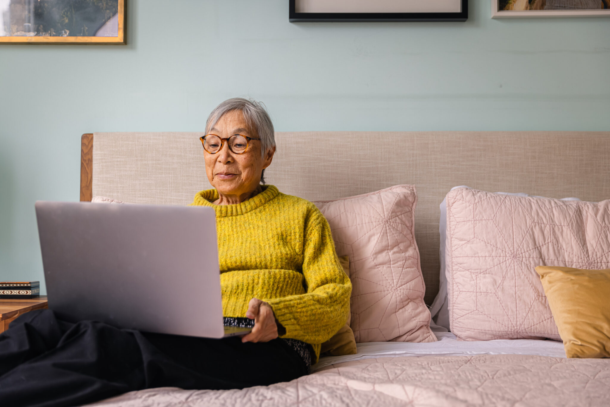 Senior asian woman using laptop while sitting in bedroom at home