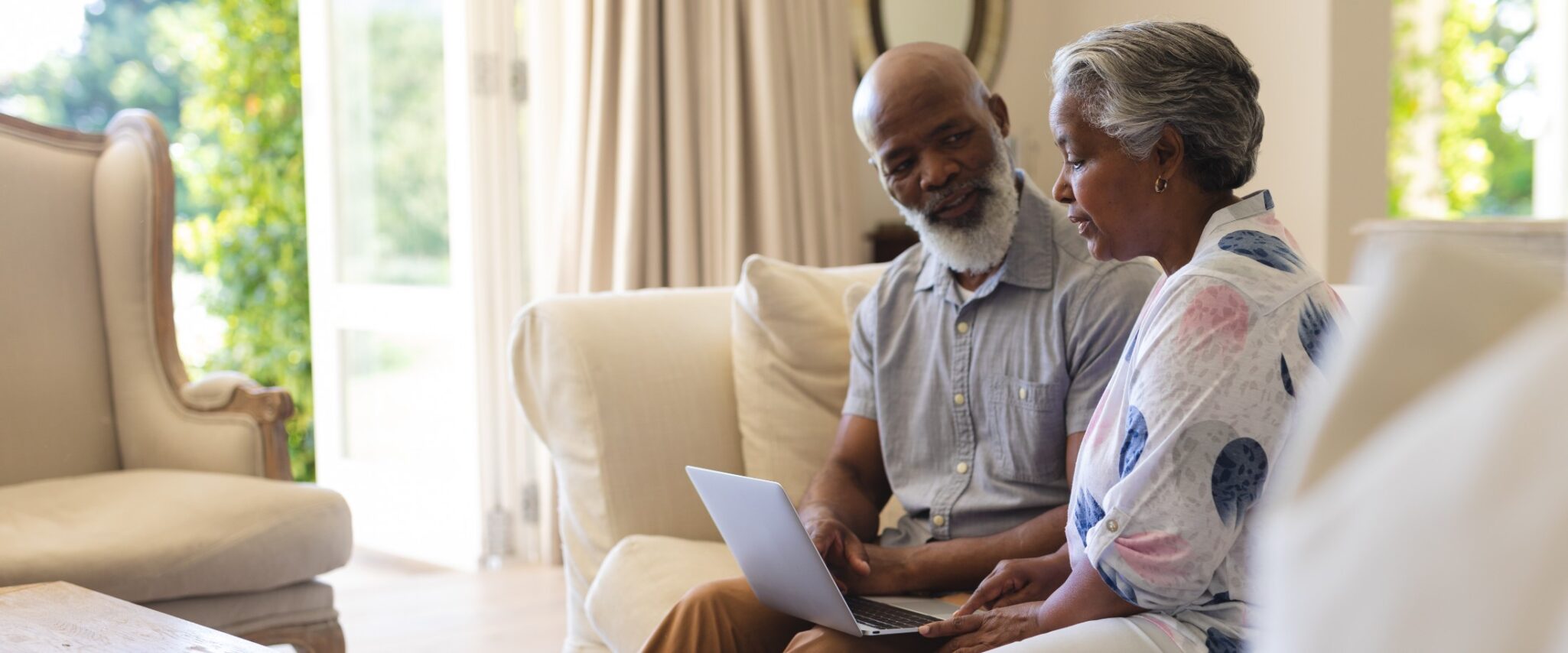 A senior african american man and woman sit on a couch together while looking at a computer.