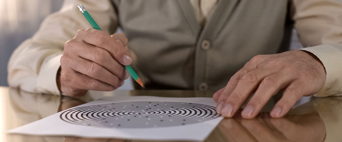 A senior man uses a pencil to work on a maze puzzle