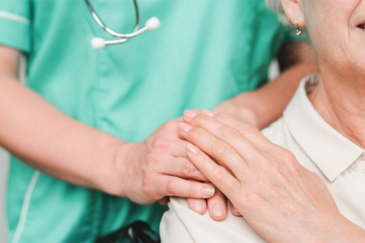 Close up of a nurse's hands on a senior resident's shoulder