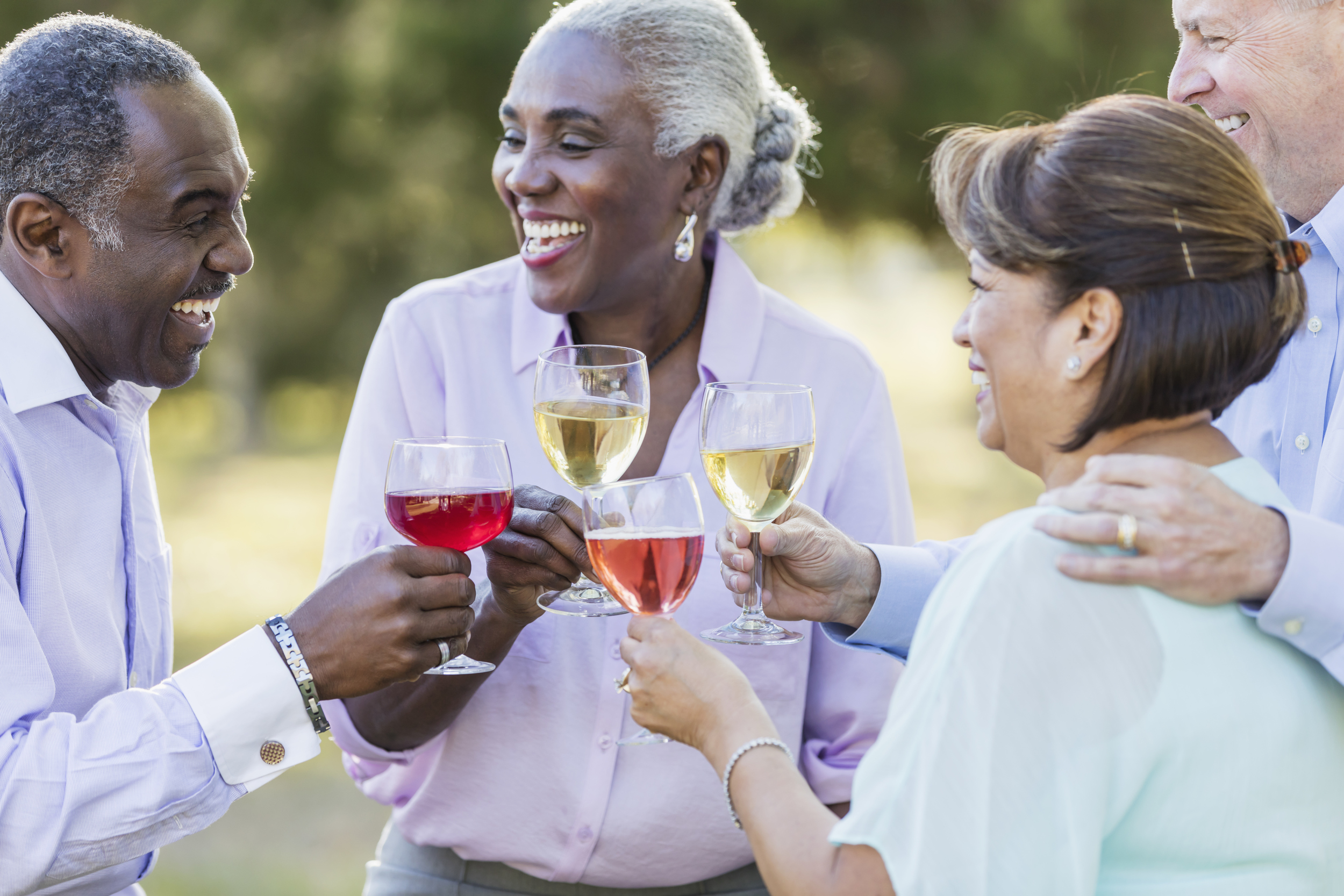 Group of senior friends talking outside while toasting with glasses of wine