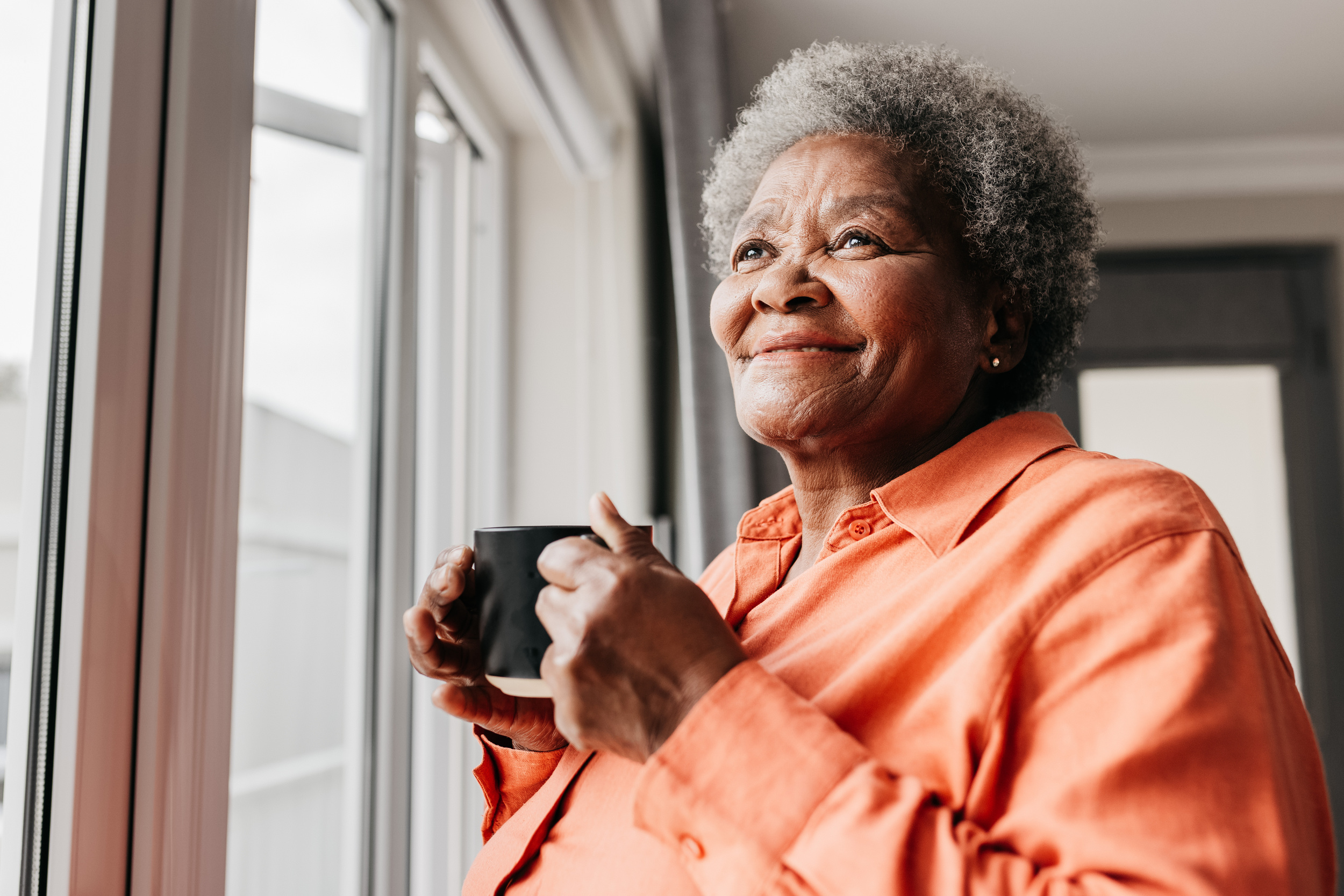 Senior woman holding cup of coffee while looking out the window