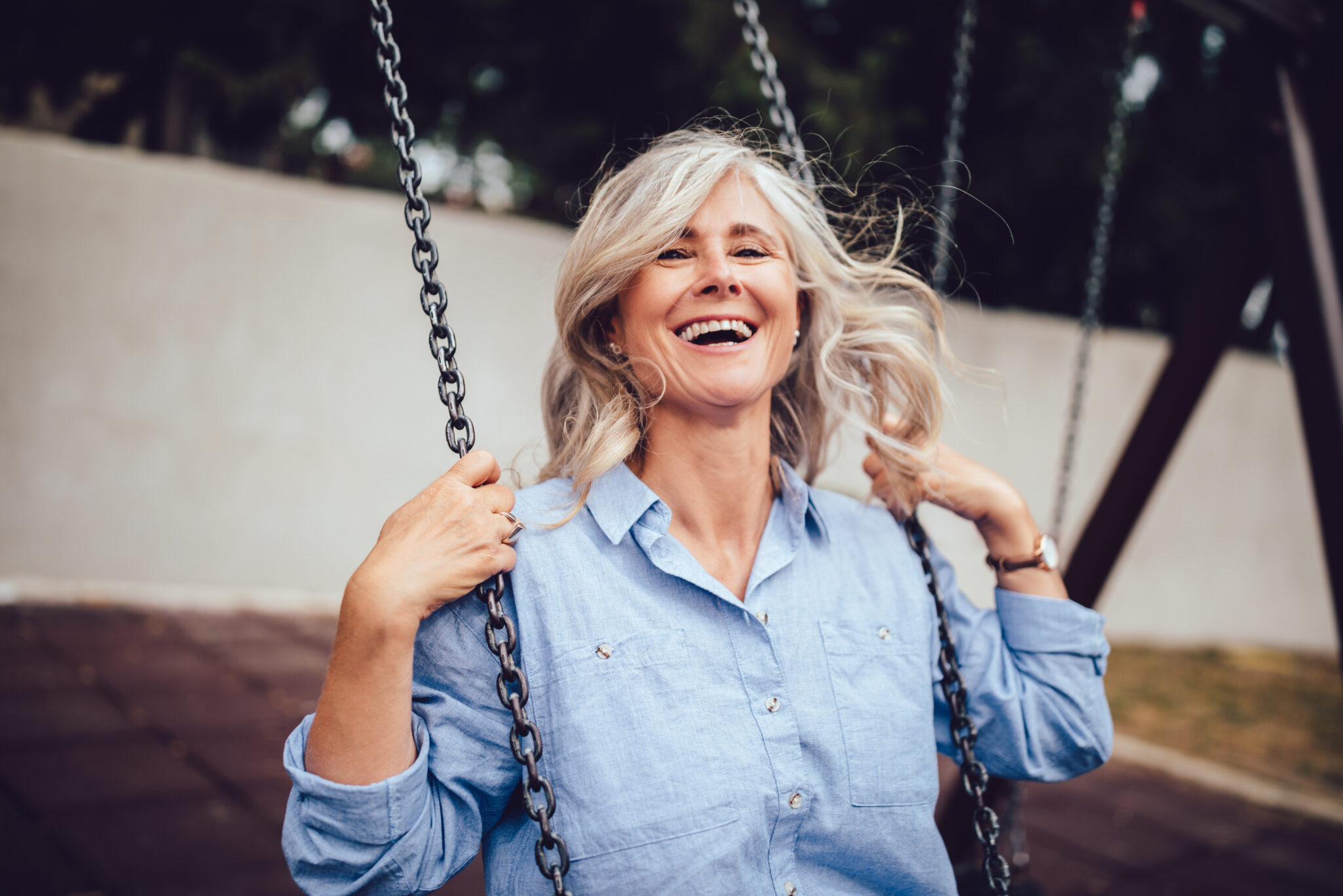 Smiling senior woman with gray hair sitting on swing, having fun and enjoying retirement