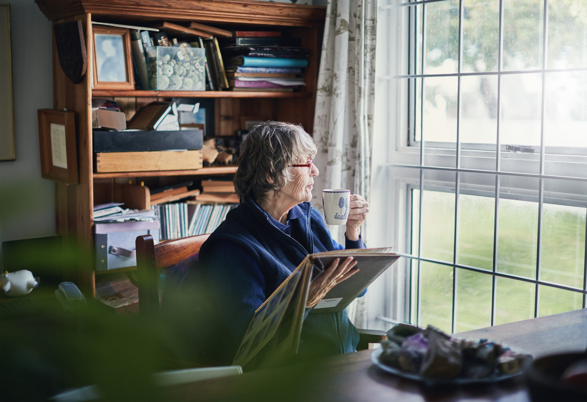 An elderly woman looks at photos while sitting next to the window